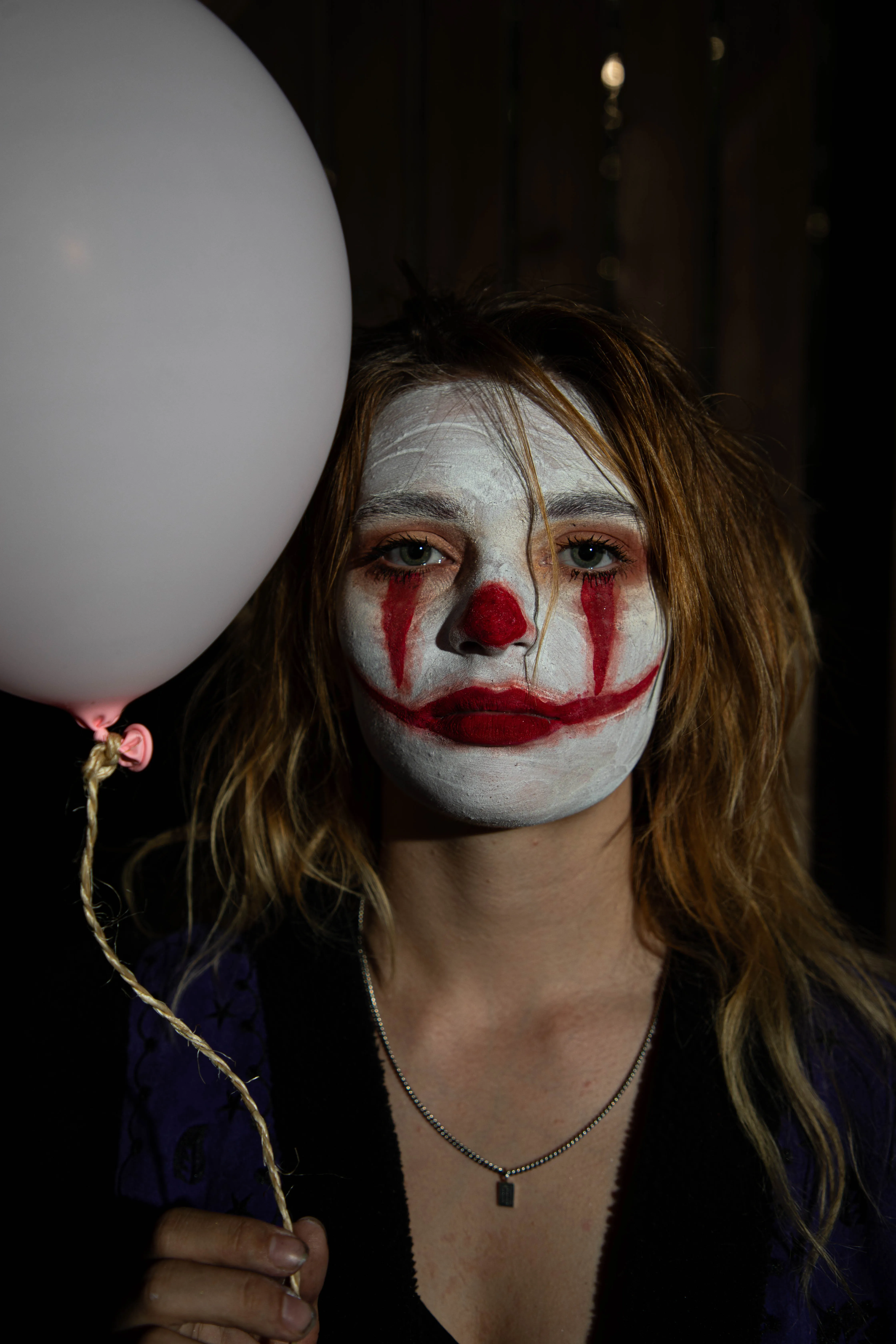 Een persoon met een clownsmasker en rode lippen, die een witte ballon vasthoudt.