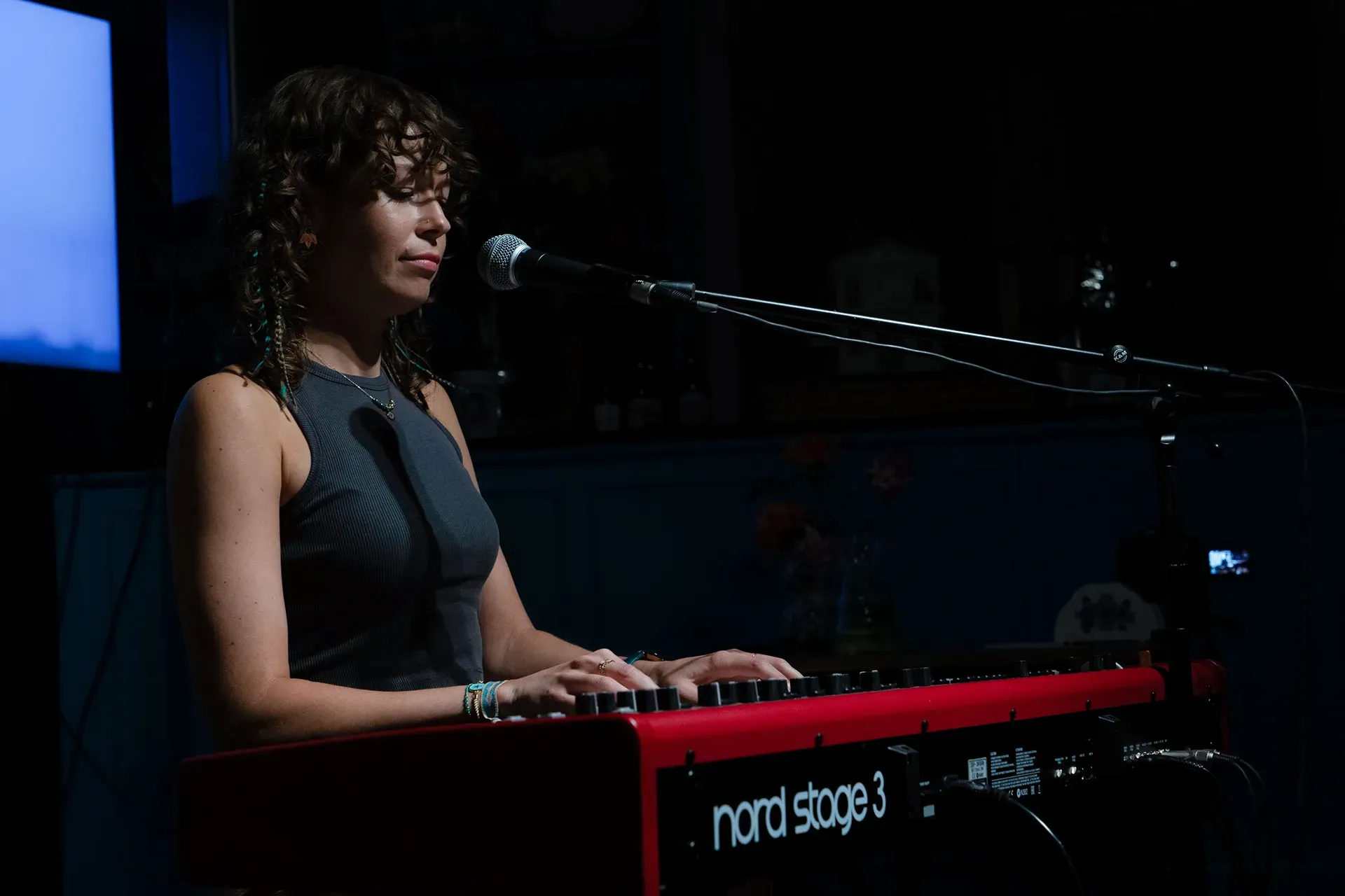 Een vrouw met krullend haar speelt op een rode toetsenbordpiano en zingt in een intieme setting.