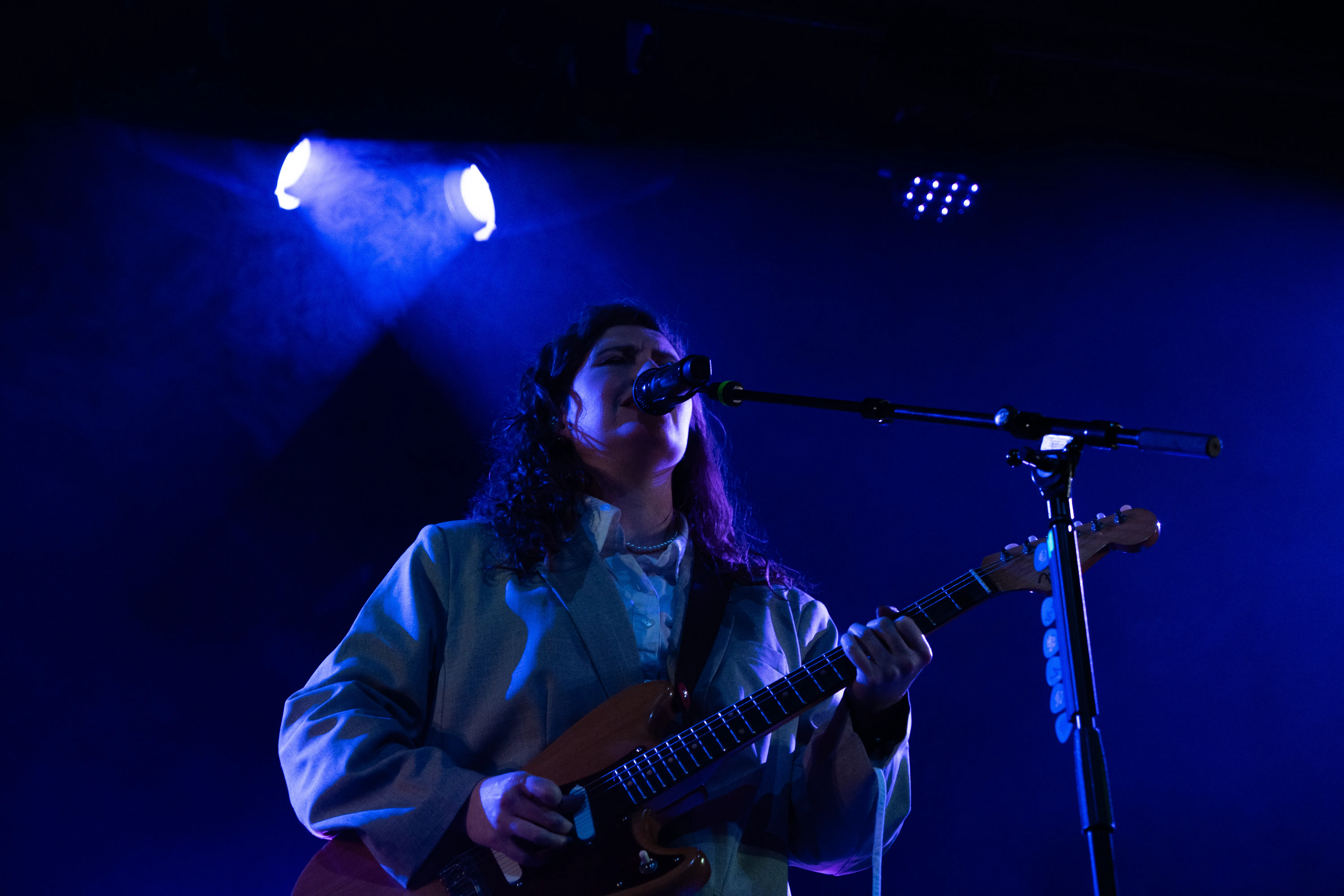 Een muzikante zingt en speelt gitaar onder een blauwe lichtshow op het podium.